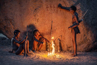 The Fire of the Ancestors Group of San tribesmen resting under an original ancient rock painting left thousands of years ago by their ancestors © Roberto Pazzi